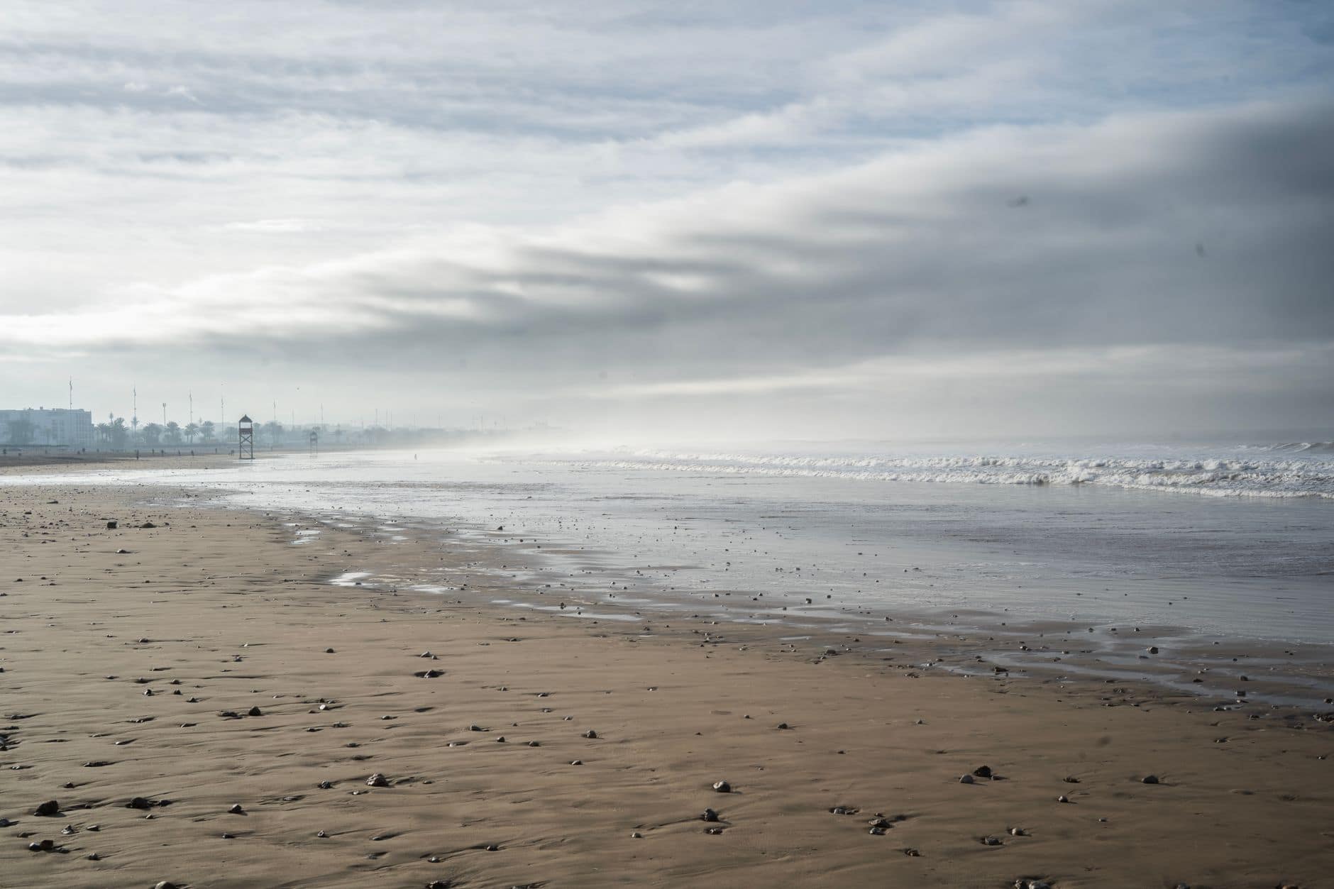 Misty morning at a deserted beach in Agadir, Morocco with gentle waves and overcast skies.