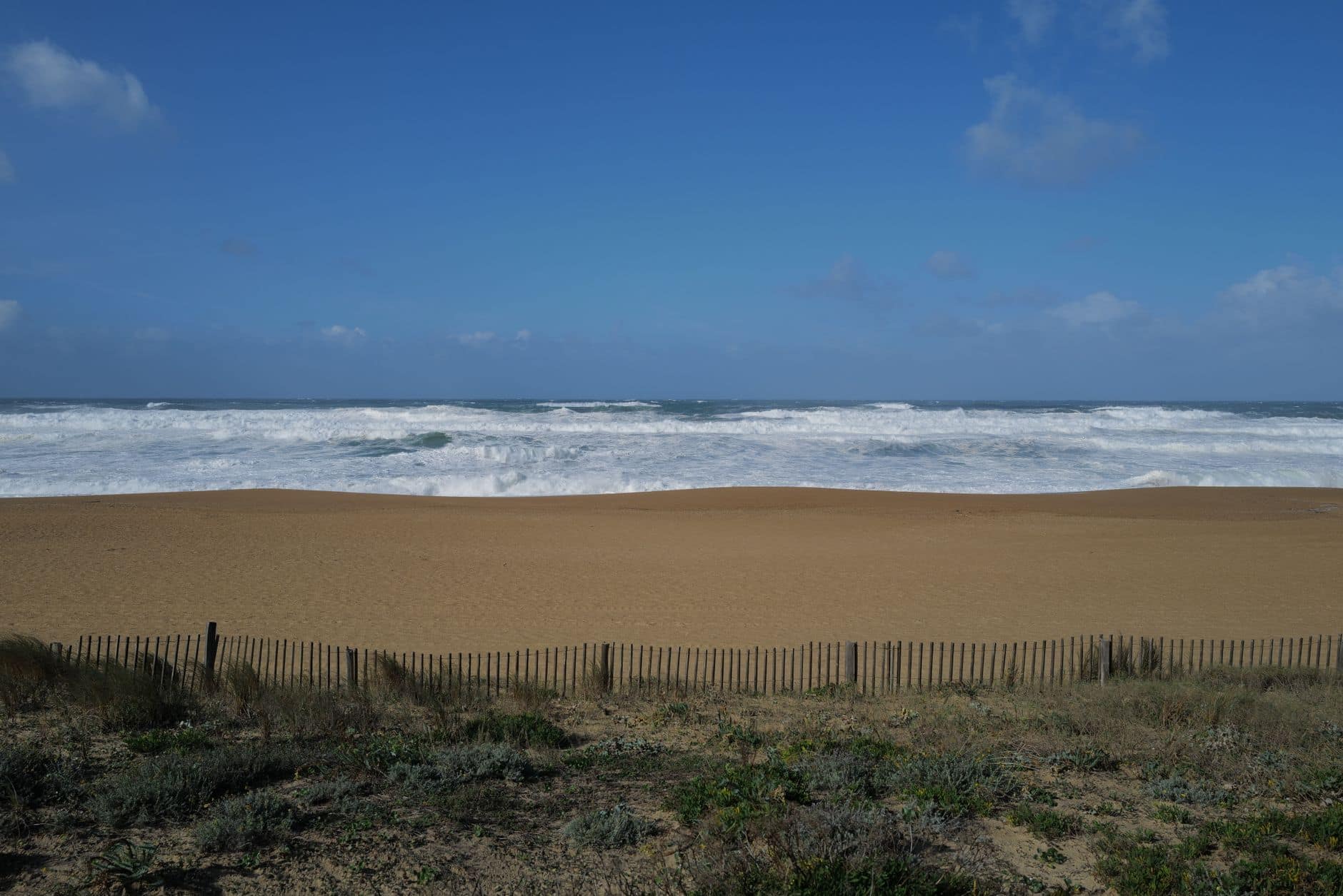 Capture of rolling waves on a sandy beach in Anglet, France, under blue skies.
