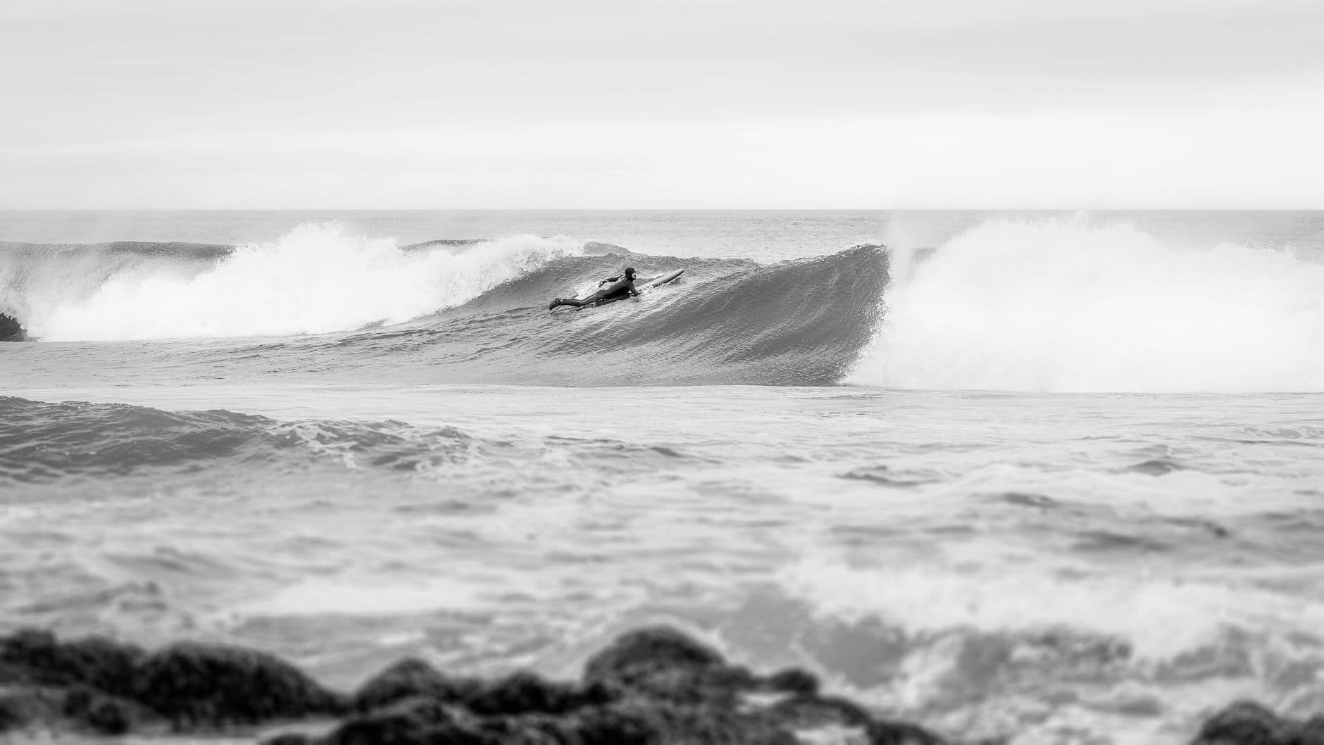 A surfer riding waves in a dramatic black and white seascape.