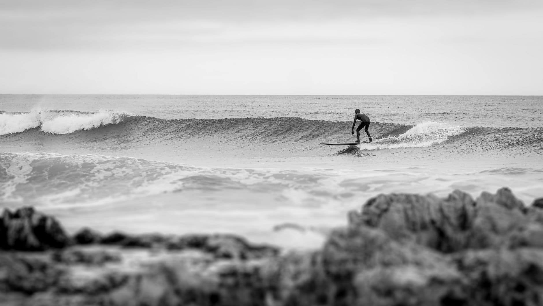 Surfer mastering the waves on a cloudy day at Uruguayana beach in a black and white image.