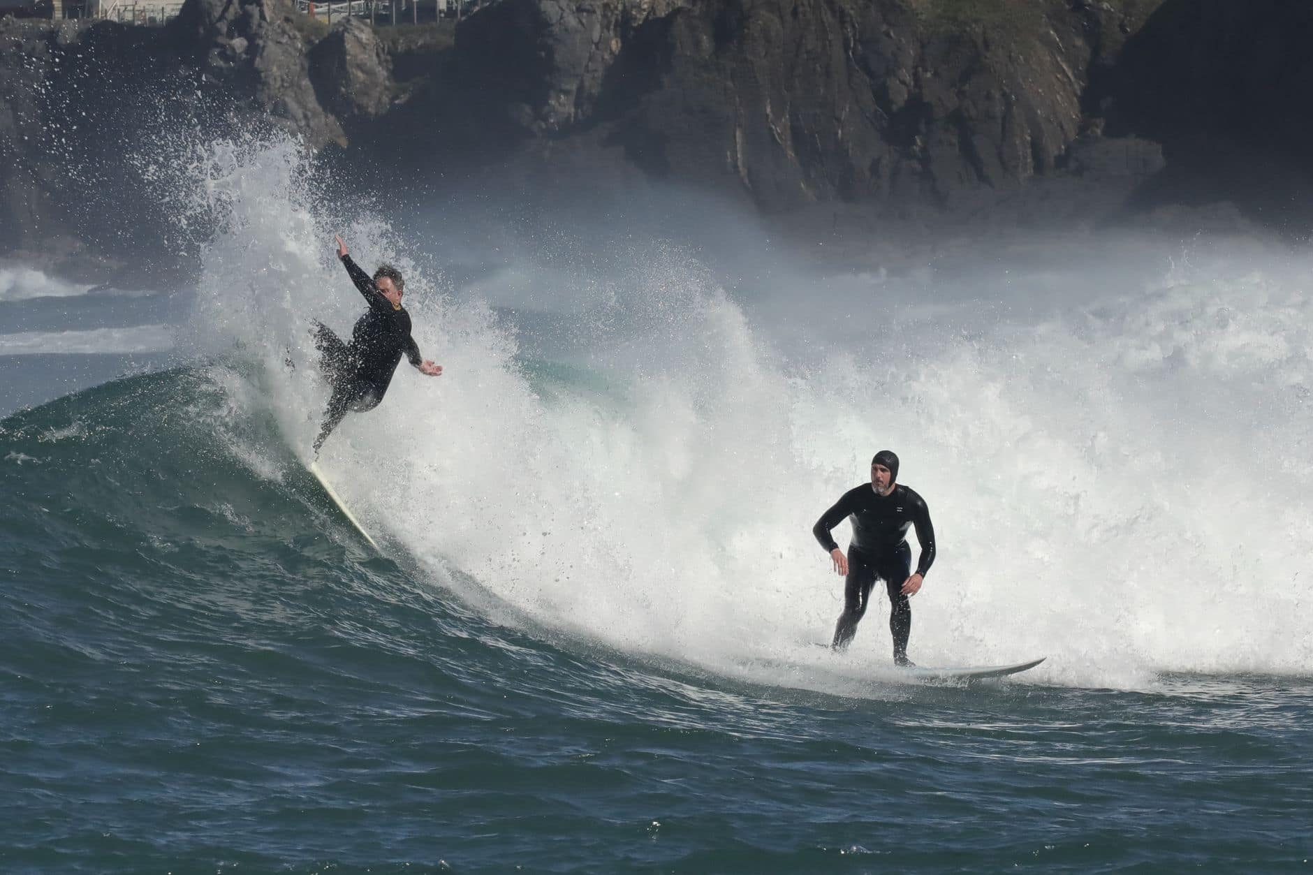 Two surfers skillfully ride big ocean waves, showcasing athleticism and thrill.