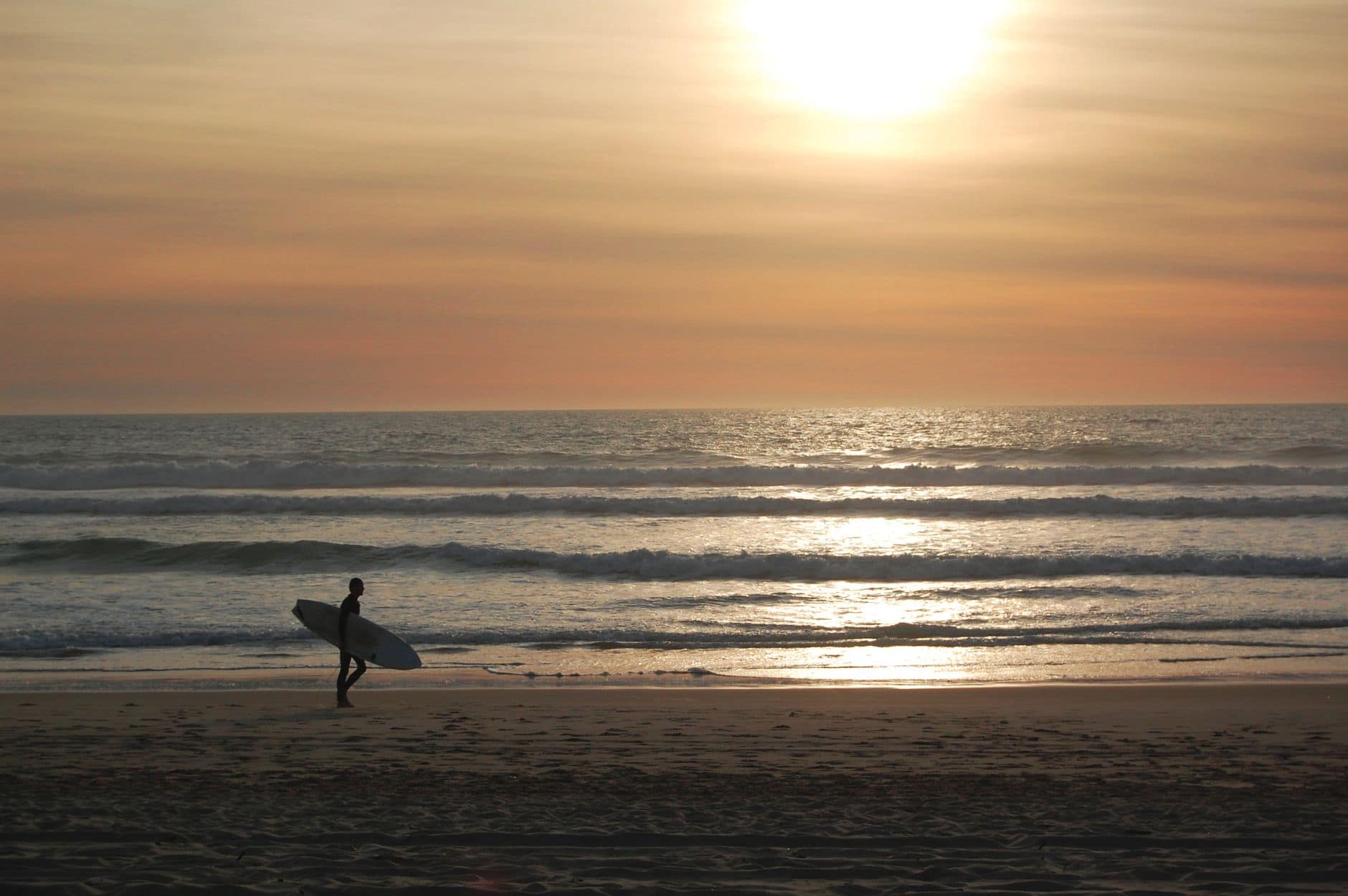 A surfer with a board walking along Mimizan beach with a stunning sunset view.