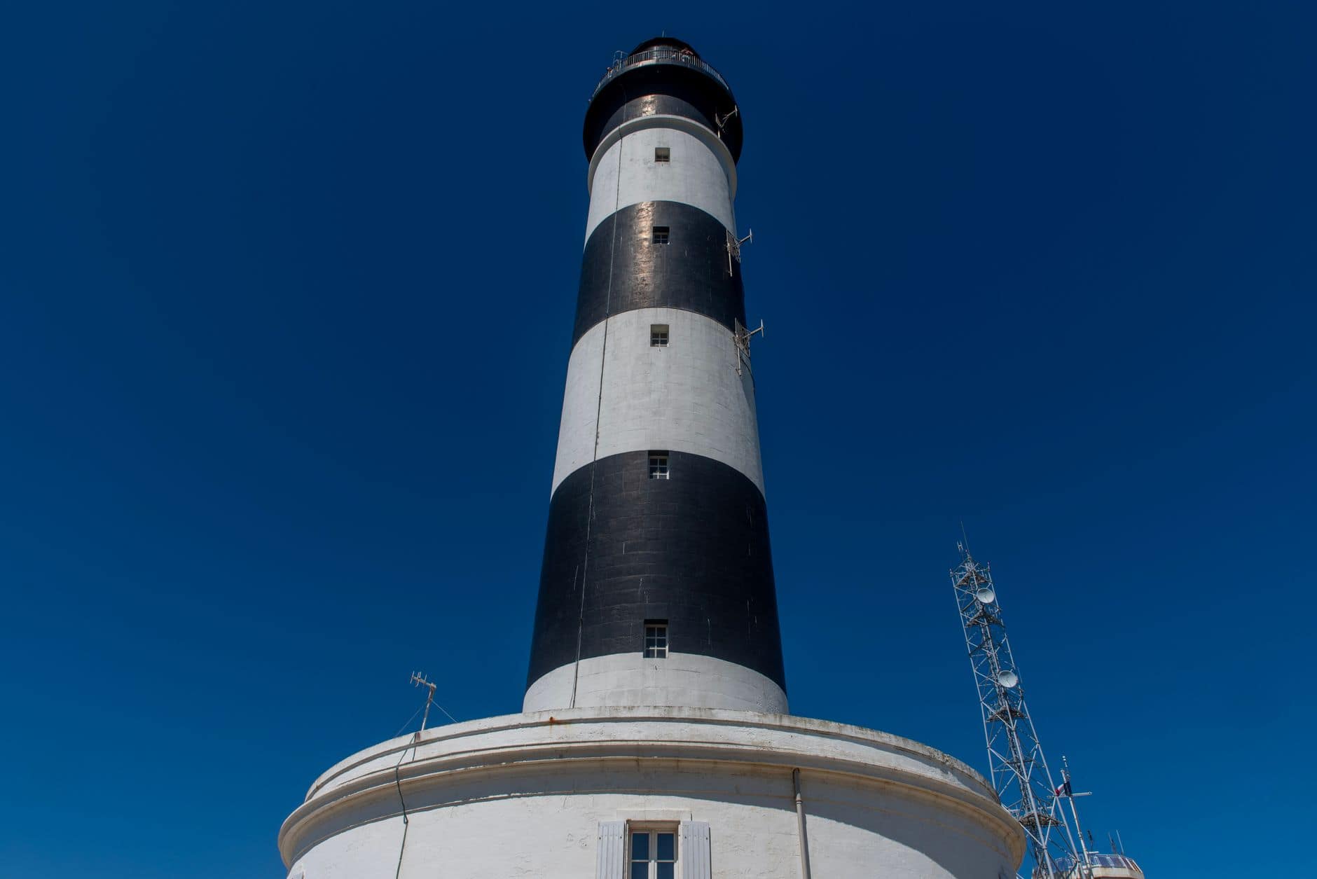Black and white striped lighthouse in Saint-Denis-d'Oléron, France, under clear blue sky.