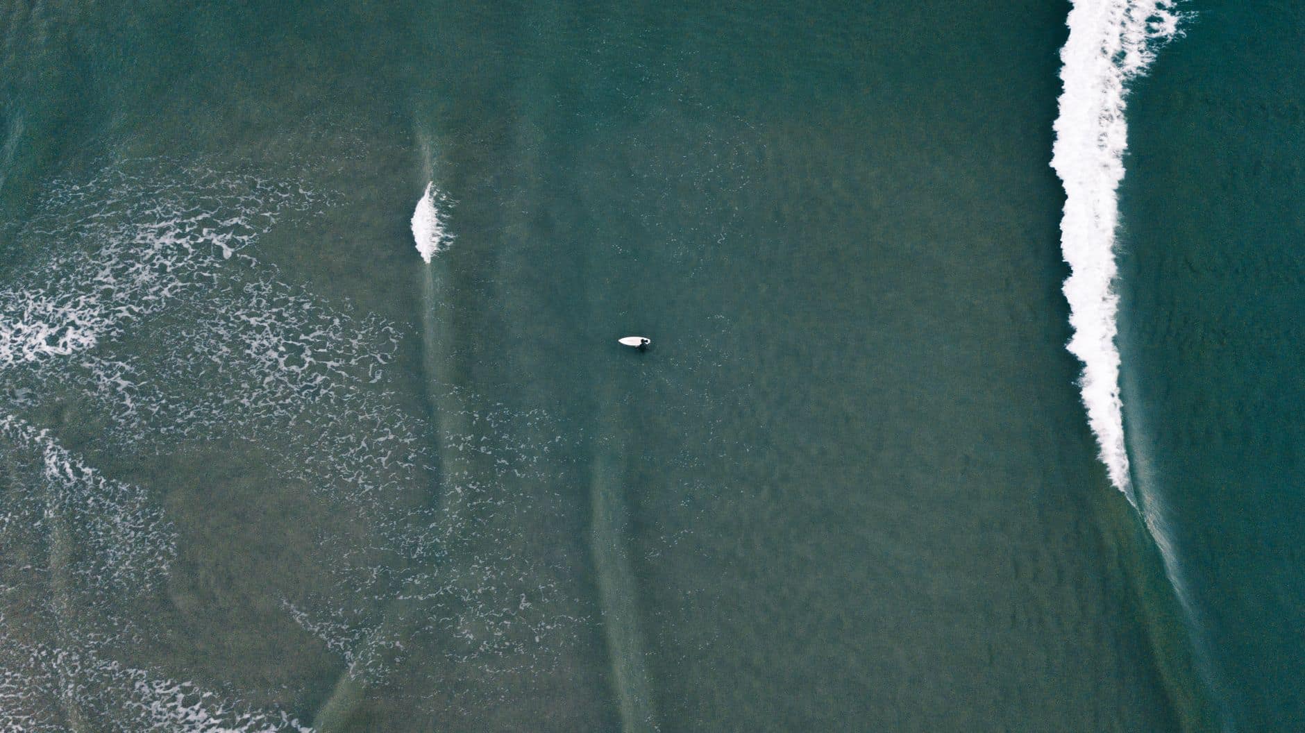 Drone shot capturing a lone surfer navigating ocean waves, perfect for beach sports themes.
