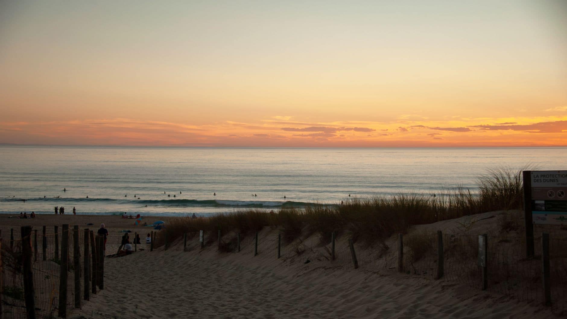 Beautiful sunset over Seignosse Beach with surfers enjoying the waves and stunning horizon views.