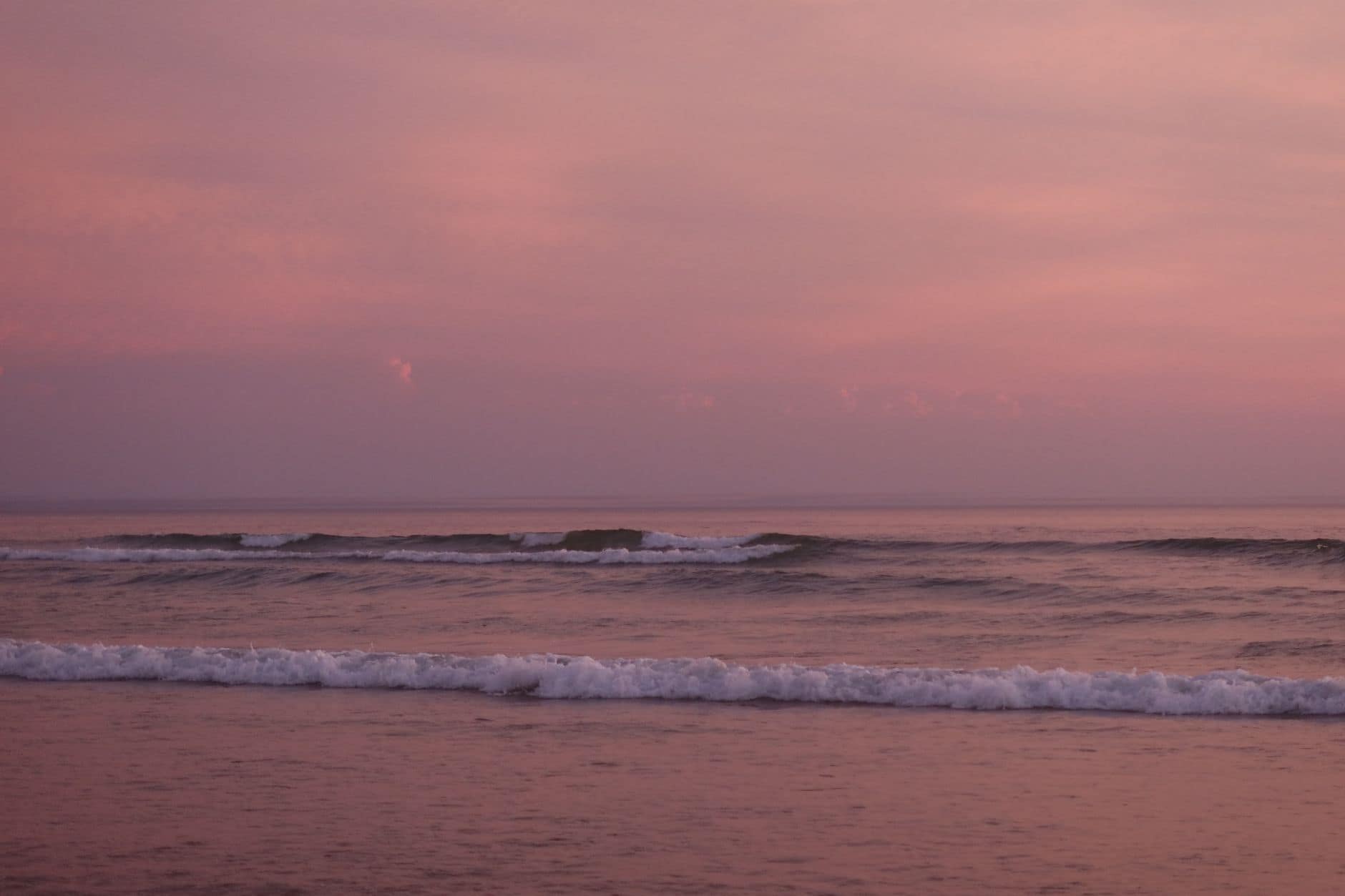 A tranquil pink sunset over the waves at Lacanau beach, creating a peaceful and serene atmosphere.