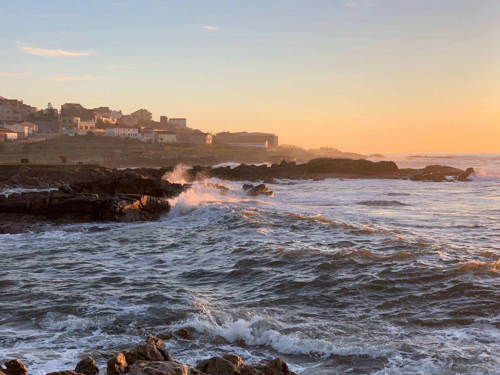 Waves crashing against rocks at sunset in Vila Praia de Âncora, Portugal, creating a scenic coastal view.